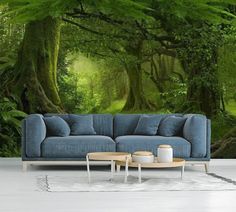 a blue couch sitting in front of a forest wall mural