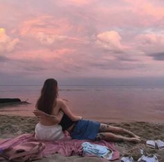 a woman sitting on top of a sandy beach next to the ocean under a cloudy sky