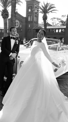 a man and woman in formal wear standing next to a car with palm trees behind them