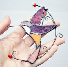 a hand holding a stained glass bird ornament in it's right hand