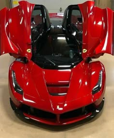 a red sports car parked in a garage with its doors open and the hood up