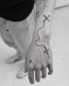 a person with a tattoo on their arm holding a cross and a beaded bracelet