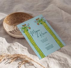 a wedding card sitting on top of a table next to a bowl and some dried grass