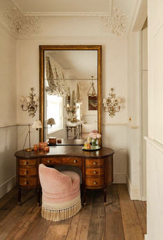 a dressing table with a mirror and pink chair in front of it on top of a hard wood floor