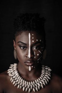 a woman with white painted on her face and necklaces around her neck is looking at the camera