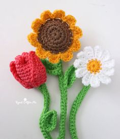 three crocheted flowers are shown on a white surface, one is red and the other is yellow