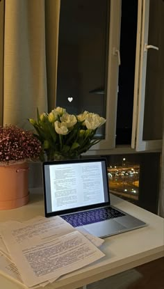 an open laptop computer sitting on top of a desk next to a vase with flowers