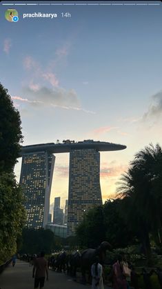 people are walking in front of some very tall buildings at sunset or dawn with the sun setting behind them