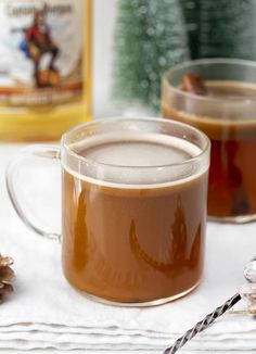 two mugs filled with hot chocolate sitting on top of a table next to pine cones