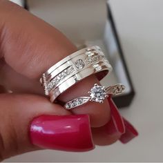 a woman's hand holding two rings with diamonds on them and a pink manicure