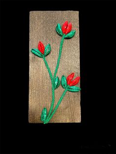 two red flowers are on a piece of wood with green stems in the shape of leaves