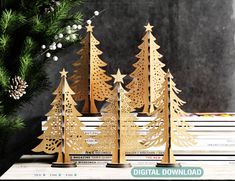 three wooden christmas trees on top of books next to a pine tree and snowflakes