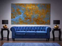 a blue couch sitting in front of a painting on a wall next to two lamps