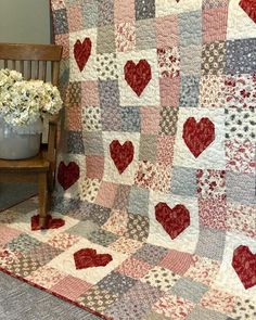 a quilt with hearts on it sitting next to a wooden chair and potted plant