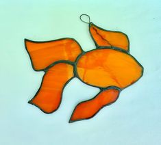 an orange stained glass fish ornament hanging on a white wall in the shape of a fish