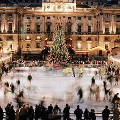 people skating on an ice rink in front of a large building with a christmas tree