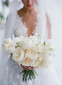 a bride holding a bouquet of white flowers in her wedding dress, wearing a veil