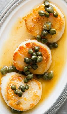 three scallops with capers and mustard in a bowl on top of a table