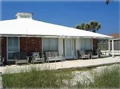 the building is white and has several chairs on it's front porch, along with palm trees