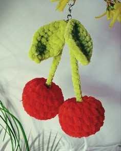 two crocheted cherries hanging from a tree branch