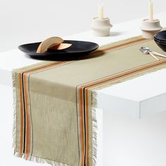 two black plates on a white table with an orange and yellow striped table runner next to them