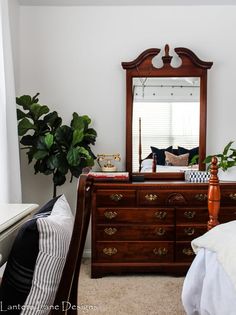 a bedroom with a bed, dresser and mirror on the wall next to a potted plant