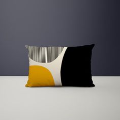 a black and yellow pillow sitting on top of a white table next to a gray wall