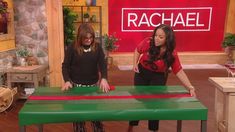 two women standing in front of a table that is painted green and red with the word rachel on it