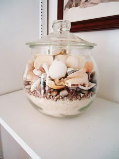 a glass jar filled with sea shells on top of a white shelf next to a mirror