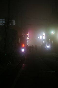 people are standing on the street at night with traffic lights in the foggy city