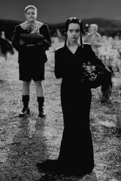 two people standing in the middle of a field wearing black clothing and holding an umbrella