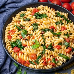 a bowl filled with pasta and spinach on top of a blue cloth next to tomatoes