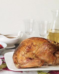 a whole turkey on a plate with wine glasses and strawberries in the bowl next to it