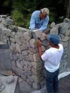 two men are working on a stone wall