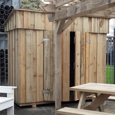 a wooden shed with two benches and a picnic table in the foreground, surrounded by wine bottles