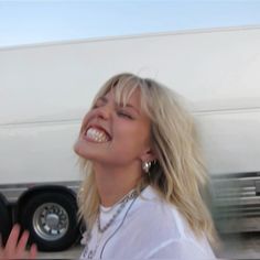 a woman is laughing while standing in front of a white truck with her eyes closed