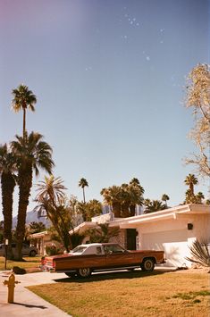 an old car parked in front of a house with palm trees and a fire hydrant