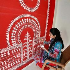 a woman sitting on a chair in front of a red wall with an intricate design