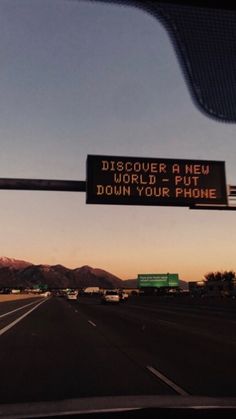 a sign on the side of a road that says, discour a new world put down your phone