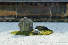 two rocks and moss in the middle of a small pond with an old building in the background