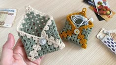 someone is holding two small crocheted purses on a table with other items