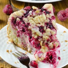 a piece of cake on a white plate with raspberries and crumbs