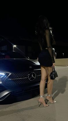 a woman standing in front of a car at night with her back to the camera