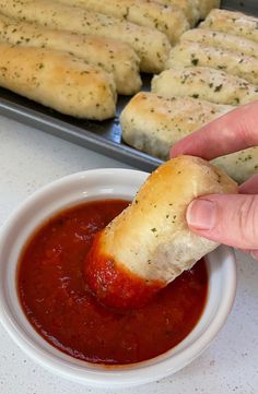 someone dipping some bread into a bowl of marinara sauce with garlic bread sticks in the background