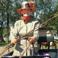 a woman in an old fashion outfit is holding a stick and sitting in the back of a horse drawn carriage