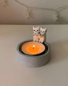 two white cats sitting on top of a table next to a lit candle in a bowl