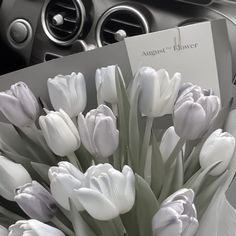 a bouquet of white tulips sitting on top of a table next to a car dashboard