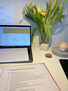 a laptop computer sitting on top of a desk next to a vase with yellow flowers