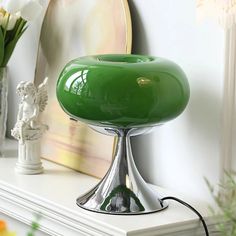 a green table lamp sitting on top of a white shelf next to a vase with flowers