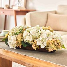 a wooden table topped with white flowers on top of a brown cloth covered table next to a couch